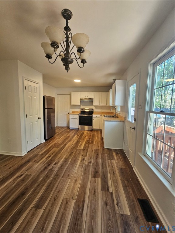 Kitchen featuring wood-finish flooring, white cabinetry, stainless steel appliances, and a decorative five-light chandelier