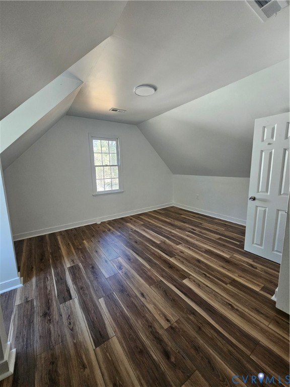 Interior room featuring vaulted ceilings, wood-finish flooring, a single-pane window, and a white six-panel door