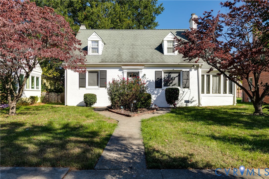 Cape Cod exterior featuring painted brick masonry, two dormer windows, dark exterior shutters, and a central chimney