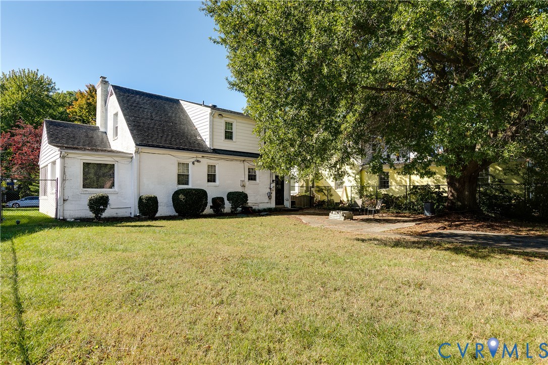 White exterior residence featuring a steeply pitched roofline, exterior brick construction, a rear patio area, and mature trees on the grounds