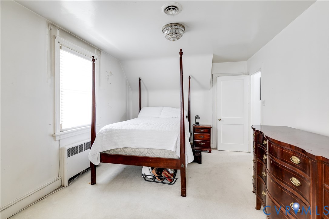 Bedroom featuring neutral wall-to-wall carpeting, sloped ceiling architecture, single-panel interior door, and a multi-pane window