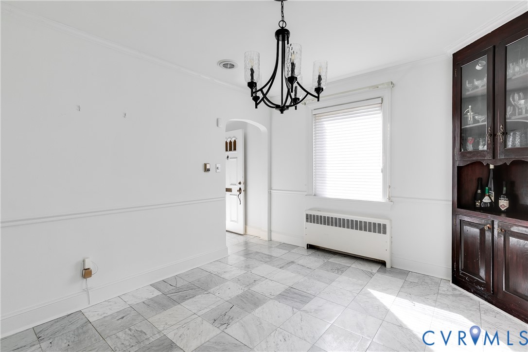 Interior space featuring tile flooring, built-in dark wood cabinetry, a decorative chandelier, and crown molding