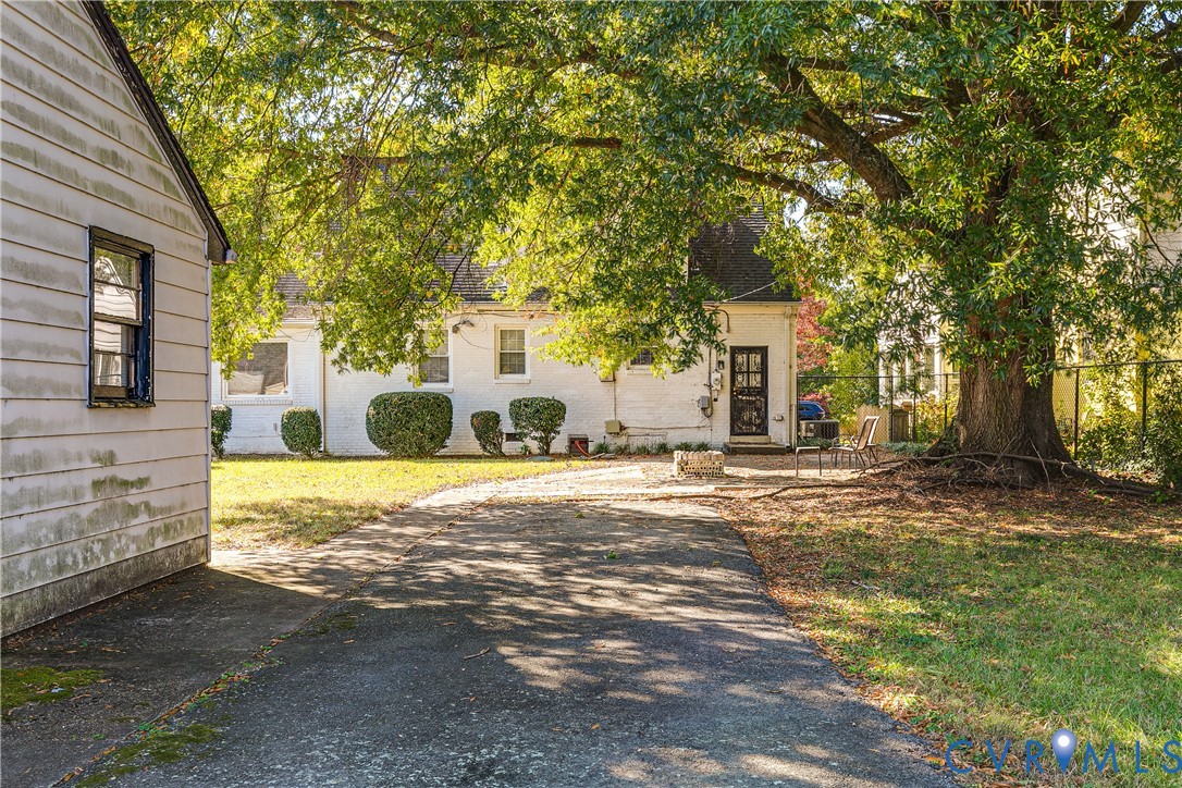 White-painted brick exterior featuring a multi-pane glass door, paved driveway, stone fire pit, and mature shade tree