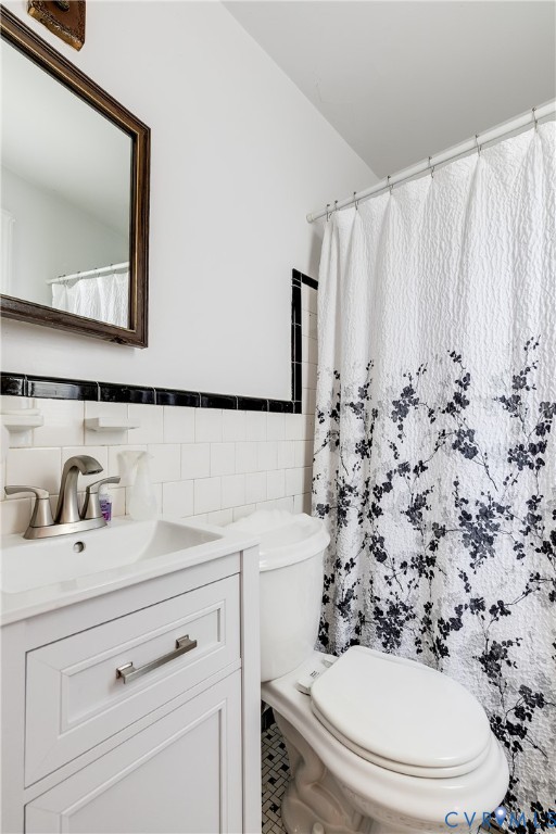 White vanity cabinet featuring a metallic finish faucet, wall-mounted mirror with a wood-tone frame, white wall tiling with black accent trim, and patterned tile flooring