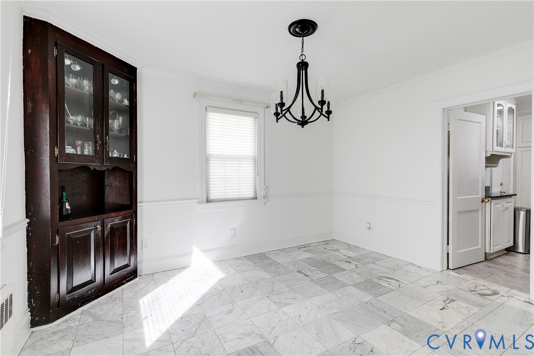 Built-in dark wood hutch, stone tile flooring, traditional black metal chandelier, and chair rail molding