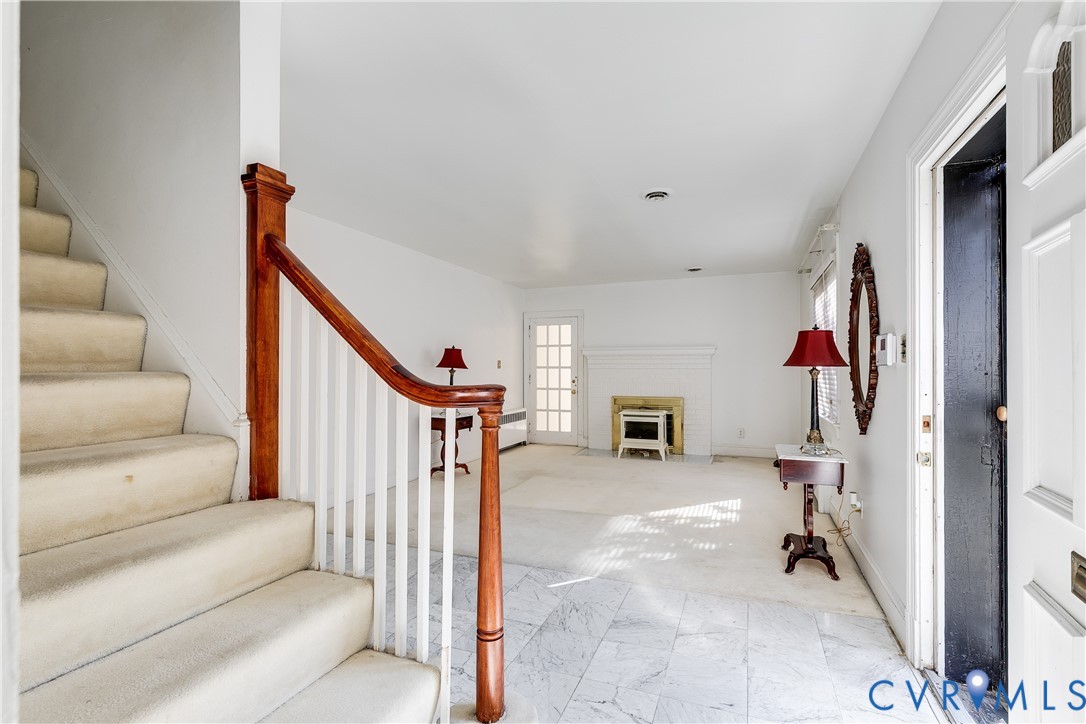 Entryway featuring stone-finish tile flooring, a staircase with a stained wood handrail, white spindle balusters, and a fireplace with a masonry hearth Entryway featuring stone-finish tile flooring, a staircase with a stained wood handrail, white spindle balusters, and a fireplace with a masonry hearth