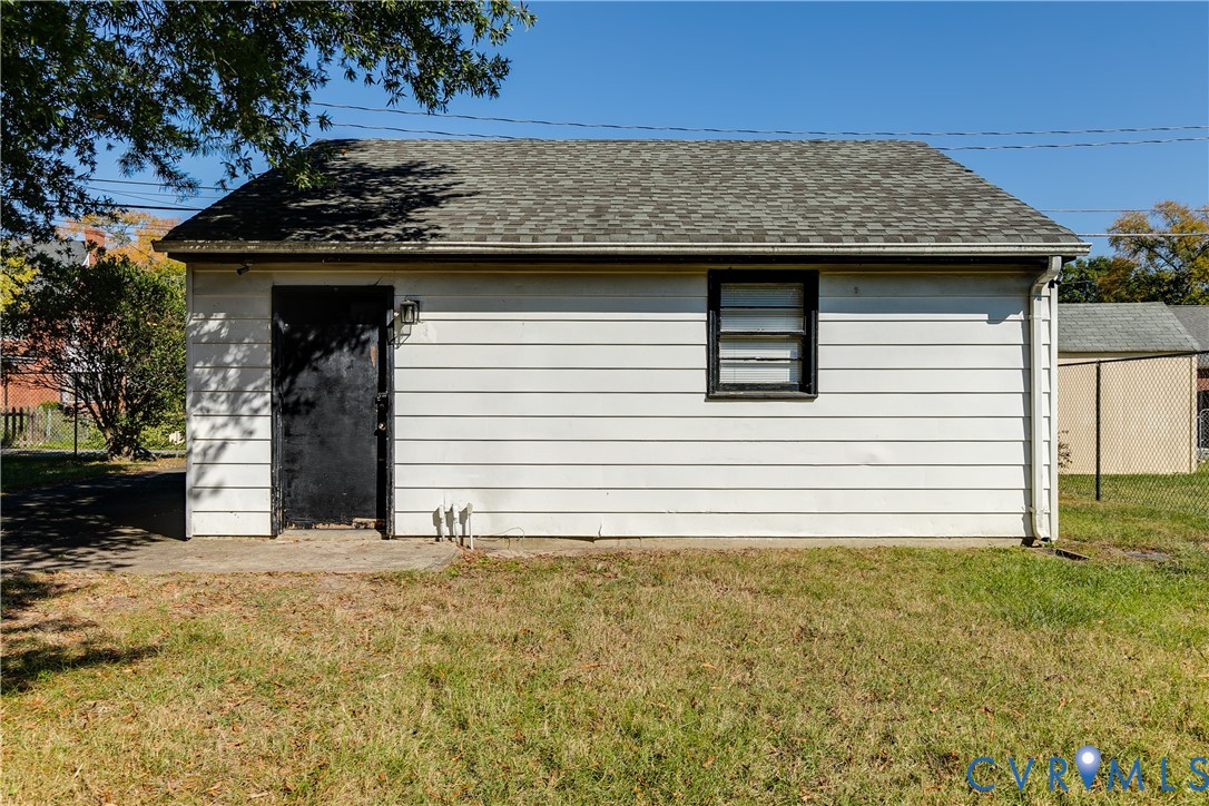 Detached structure featuring white horizontal siding, an asphalt shingle gable roof, and a single-entry door with exterior sconce lighting