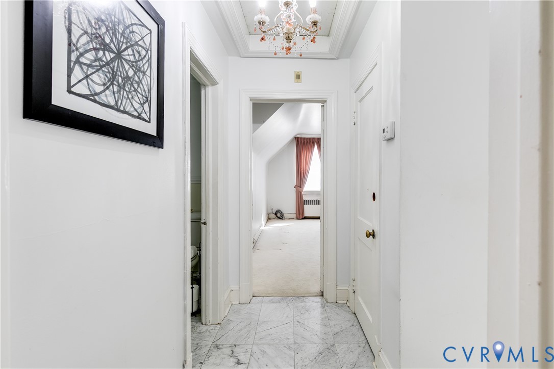 Hallway featuring marble tile flooring, a multi-tiered ceiling-mounted chandelier, and recessed ceiling detail