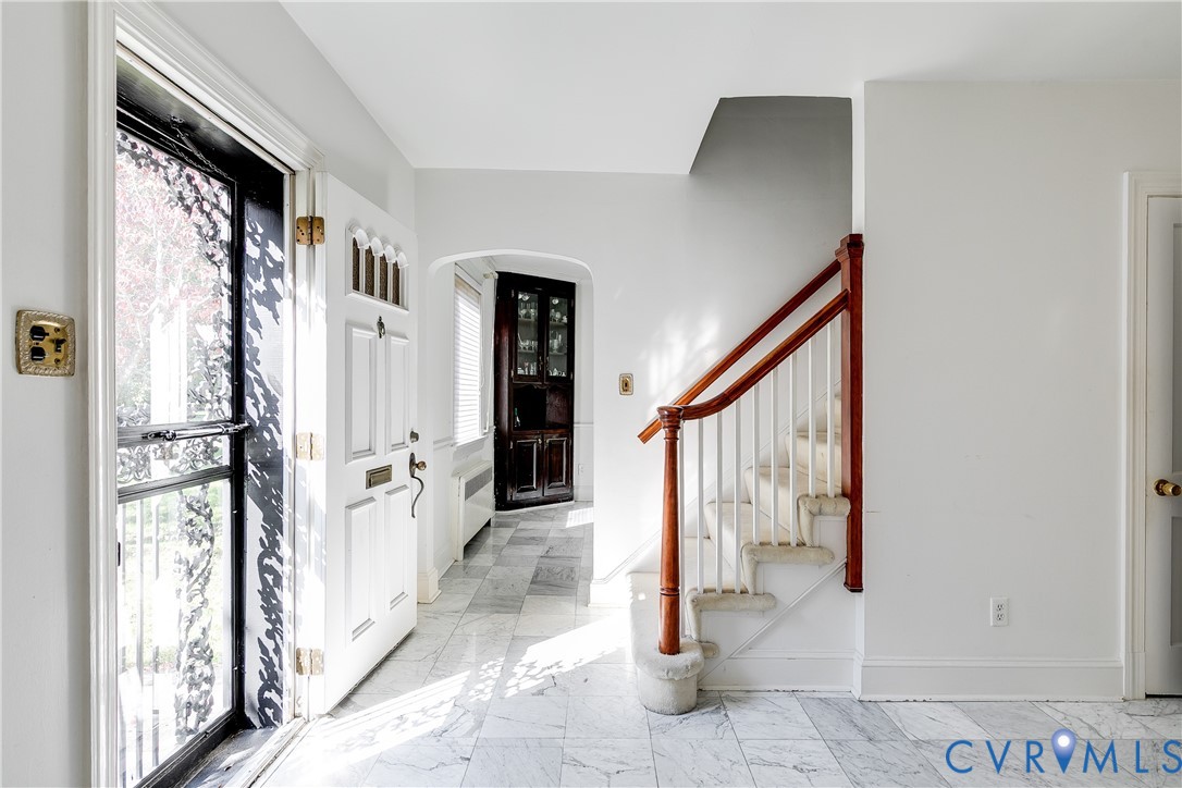 Entryway featuring stone tile flooring, a multi-paneled front door with transom detailing, a staircase with a natural wood handrail, and built-in corner cabinetry Entryway featuring stone tile flooring, a multi-paneled front door with transom detailing, a staircase with a natural wood handrail, and built-in corner cabinetry