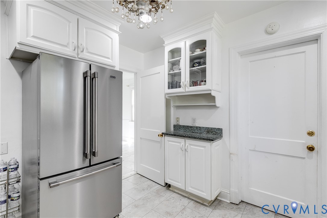 Kitchen featuring white shaker-style cabinetry, glass-front upper cabinet doors, stone-surface countertop, stainless steel refrigerator, and tiled flooring