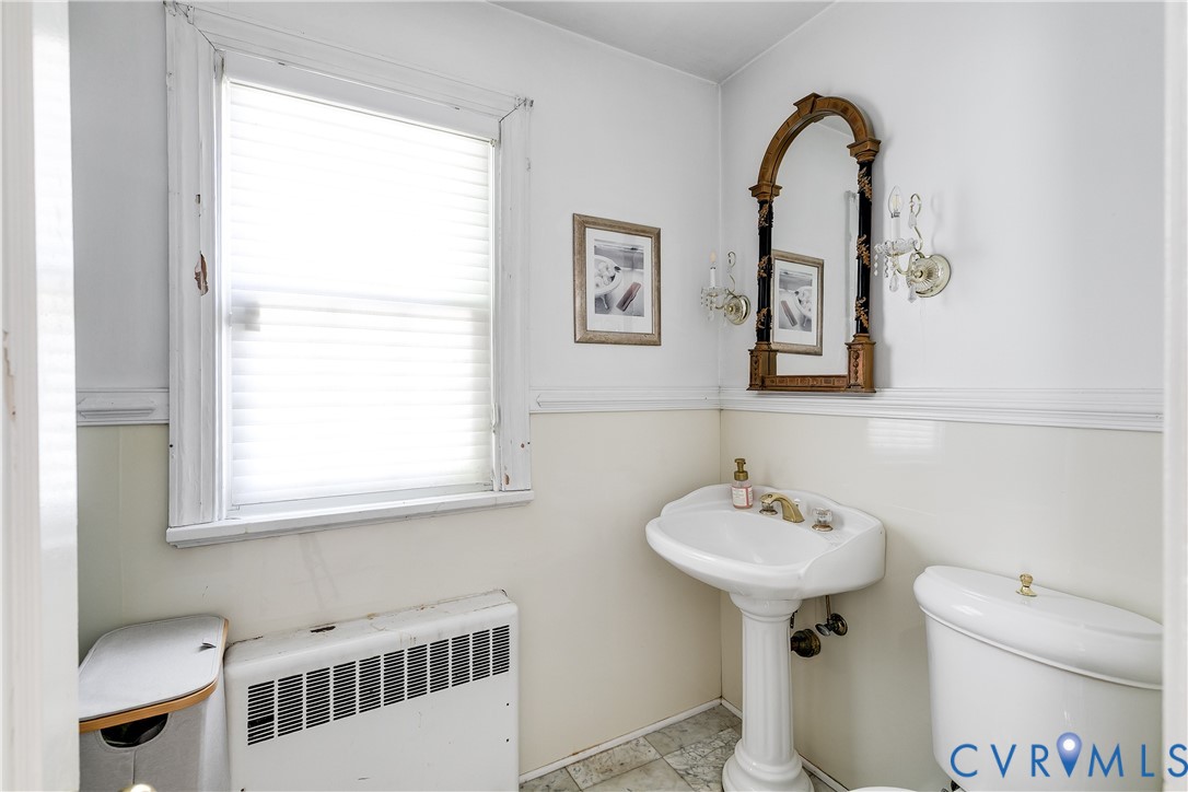 Bathroom featuring a pedestal sink, wall-mounted light fixtures, tile wainscoting, and tile flooring