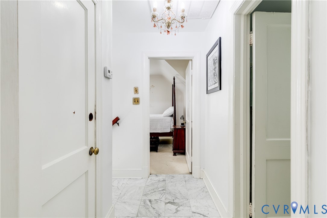 Hallway featuring stone flooring, a tiered crystal chandelier, and paneled interior doors with brass-tone hardware