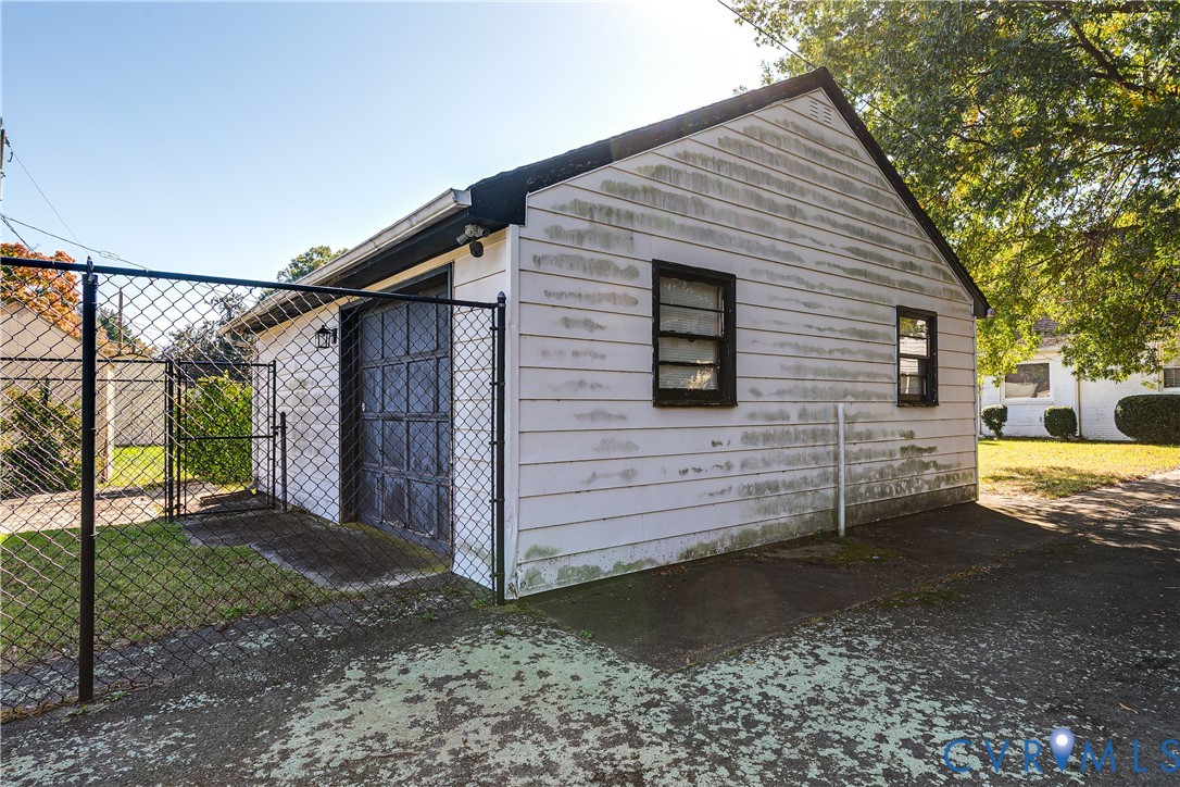 Detached garage structure featuring horizontal lap siding, a paneled overhead door, two single-hung windows, and an enclosed chain-link fence perimeter