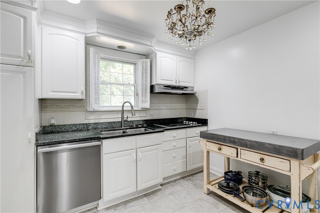Kitchen featuring white cabinetry, stone-finish countertops, stainless steel dishwasher, decorative crystal chandelier, and tiled flooring
