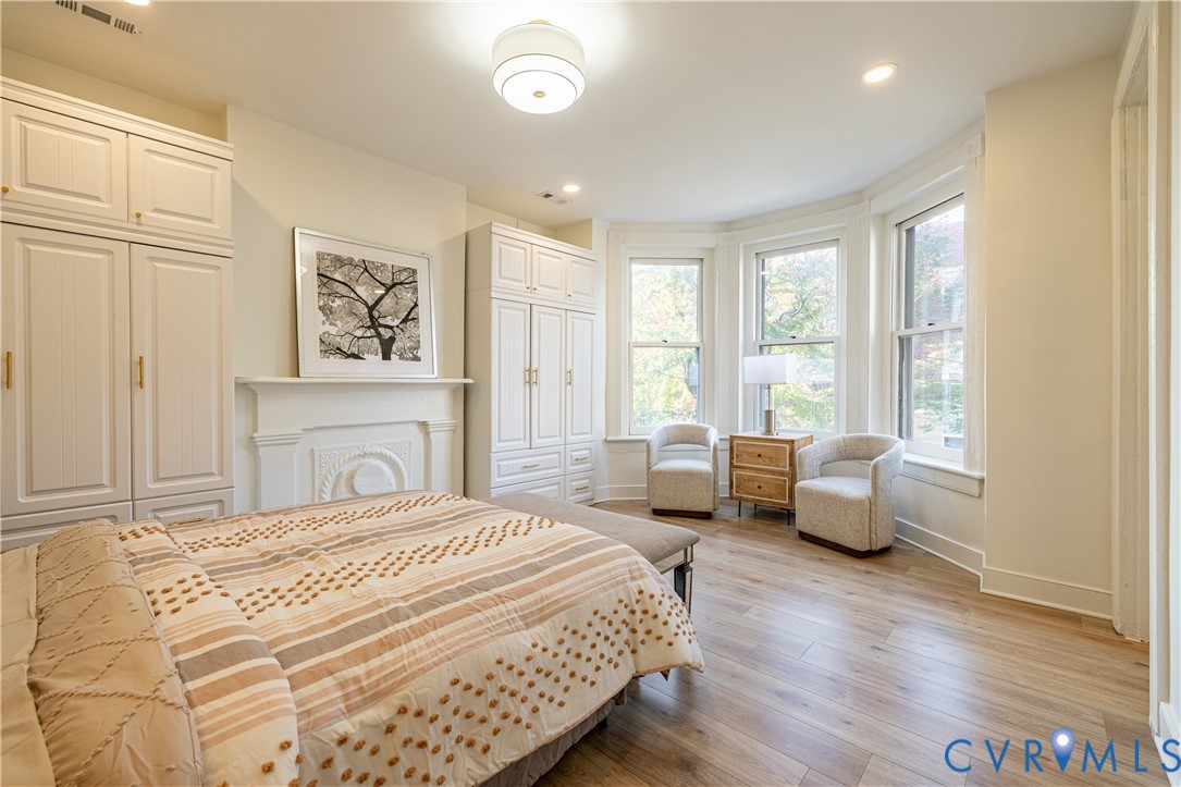 Wood-finish flooring, bay windows with natural light, decorative fireplace mantel, and built-in cabinetry with hardware finishes