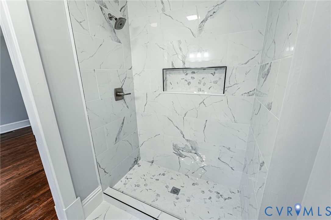 Walk-in shower featuring large-format tile surround with a veined pattern, built-in recessed wall niche, brushed-finish fixtures, and a coordinating tiled floor