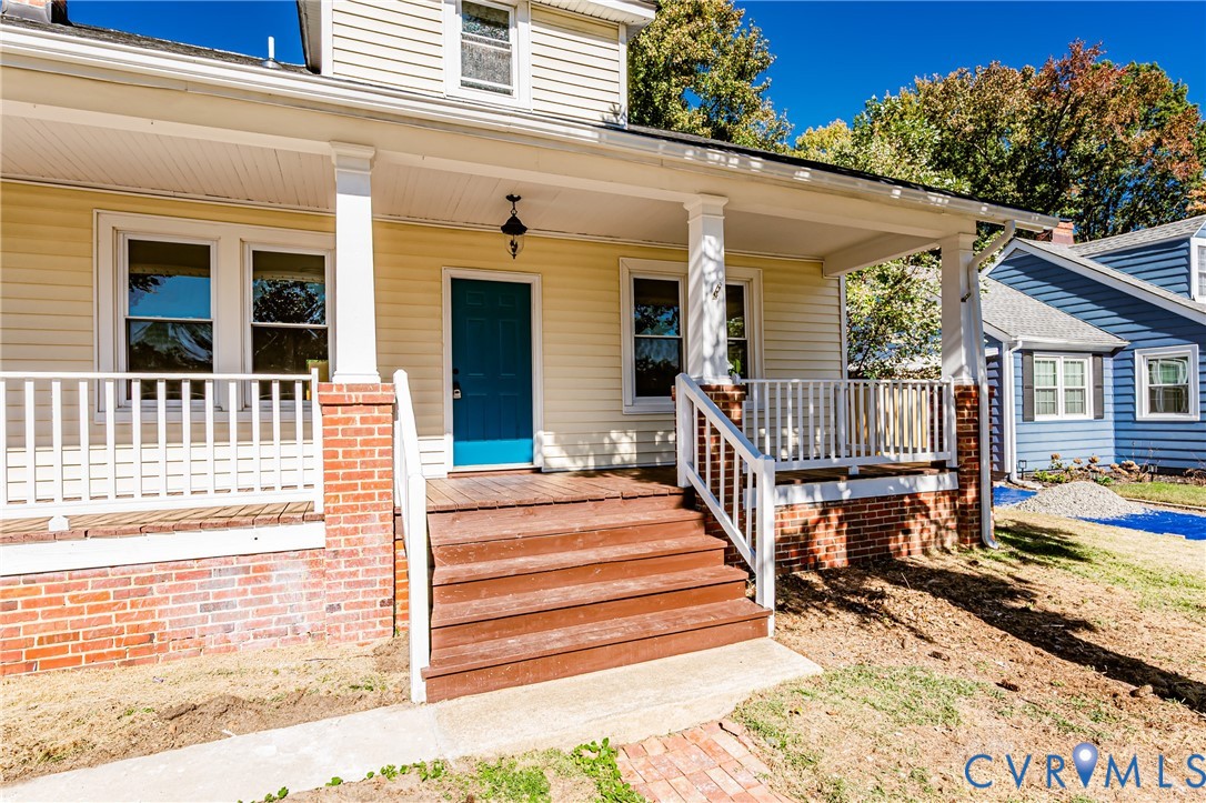 Covered front porch featuring brick-based columns, wood-finish stairs, white railings, and a solid-color front door