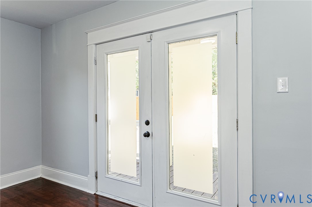 Double glass-paneled entry doors featuring white casing, dark hardware, and wood-finish flooring