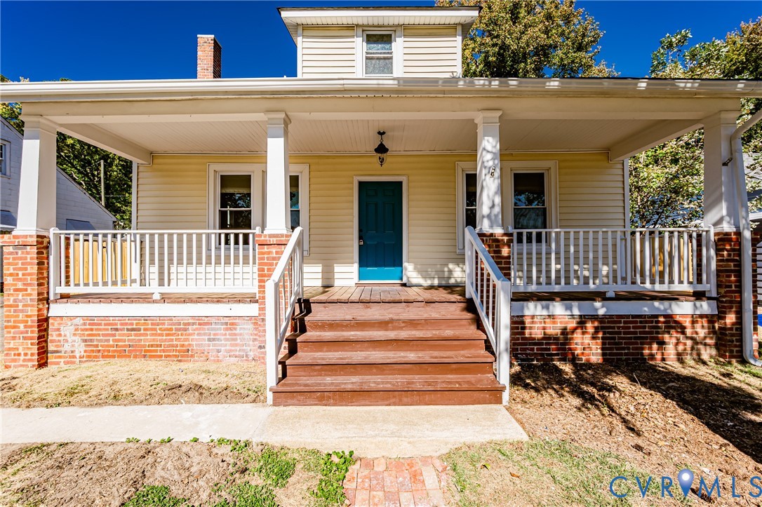 Covered front porch featuring brick-base columns, white wood railings, a central wooden staircase, and a masonry chimney Covered front porch featuring brick-base columns, white wood railings, a central wooden staircase, and a masonry chimney