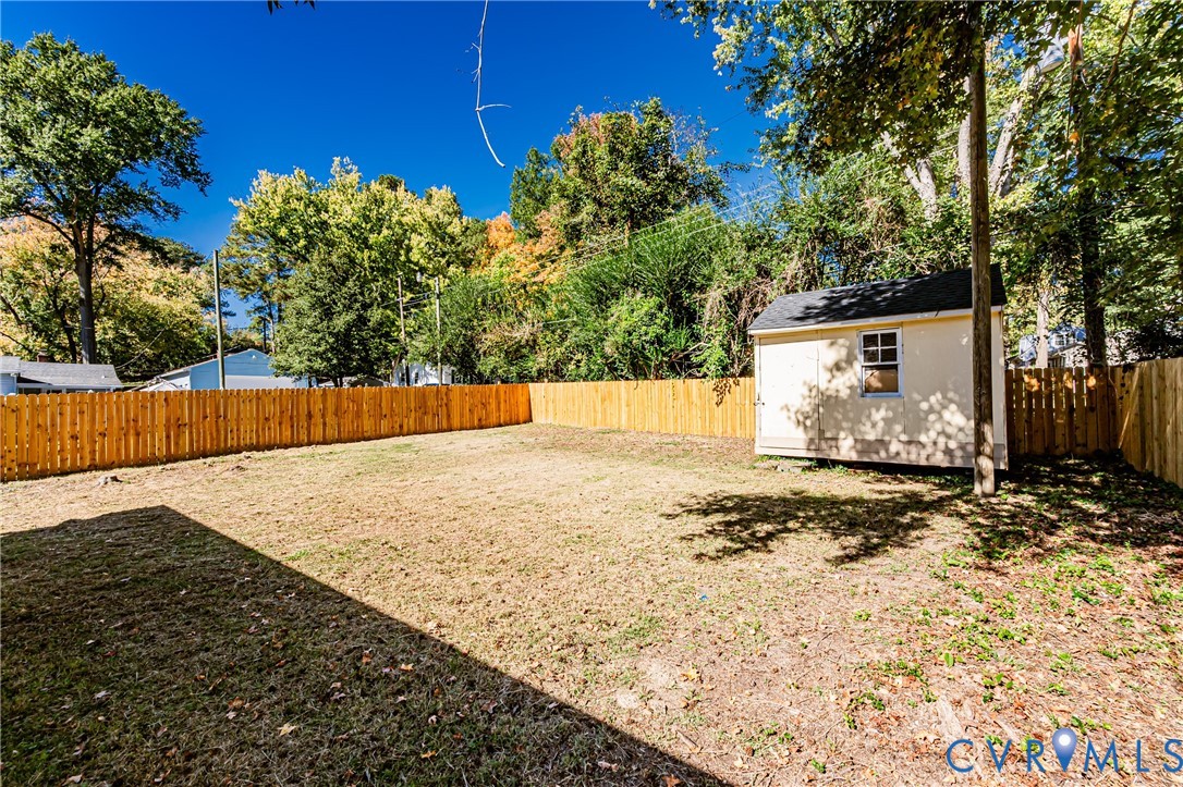 Expansive backyard featuring a wood privacy fence, detached storage shed, and mature trees