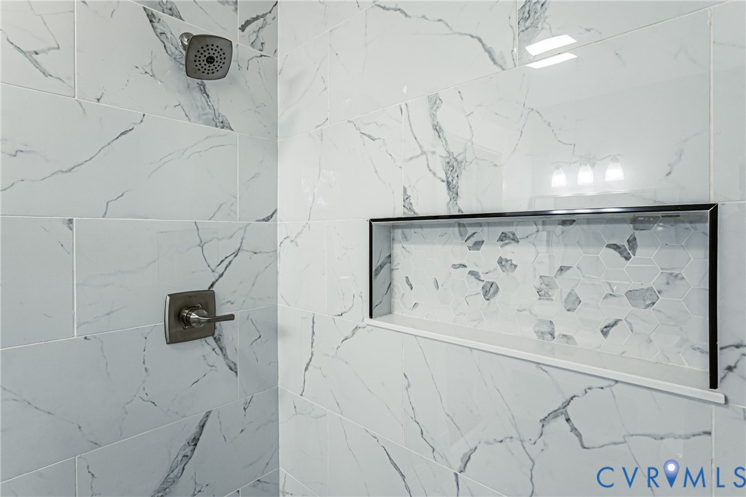 Large-format wall tiling with a vein-pattern finish, built-in recessed wall niche with hexagonal accent tile, and brushed nickel shower fixtures