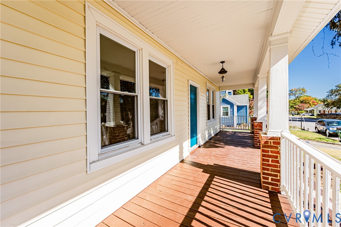 Covered porch featuring wood-finish decking, white railings, brick-based columns, and a single-light exterior pendant fixture