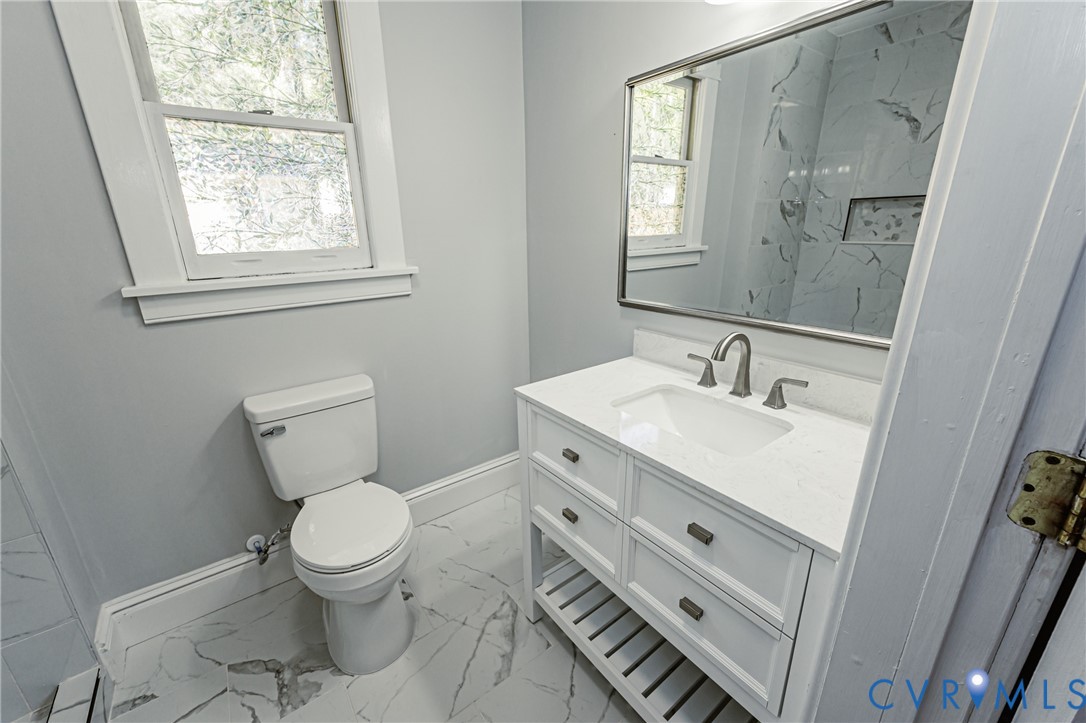 Bathroom featuring a vanity with a white composite countertop, undermount sink, brushed nickel faucet, large wall-mounted mirror, and stone-finish floor tile