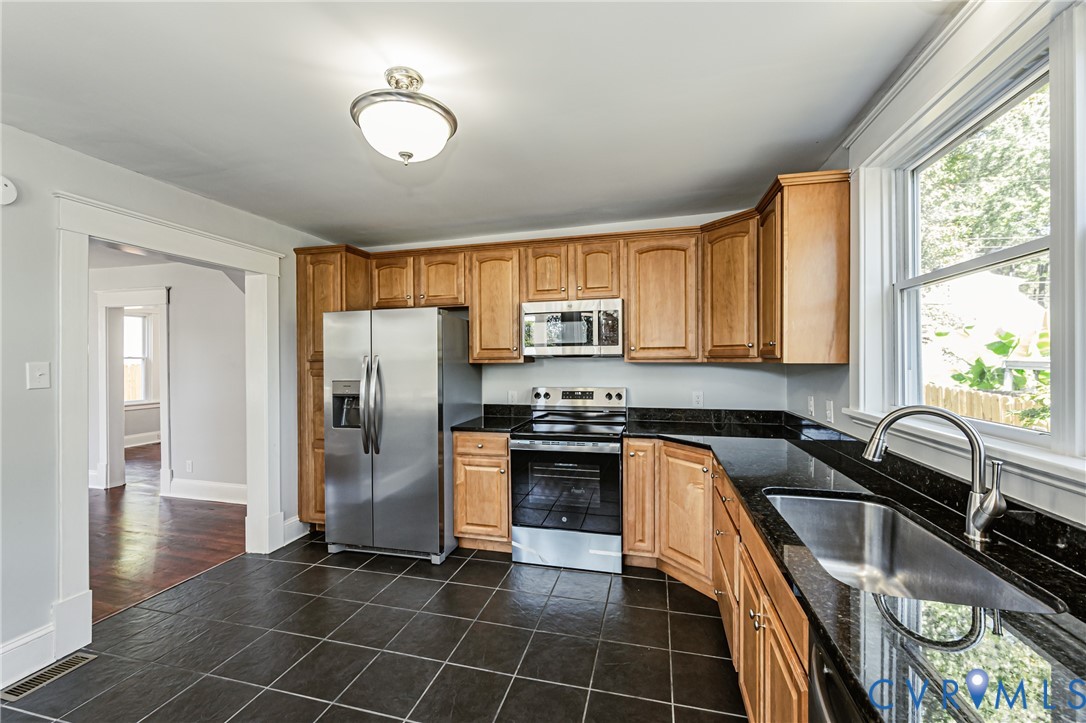 Kitchen featuring wood cabinetry, dark stone countertops, stainless steel appliances, a stainless steel undermount sink, and tiled flooring