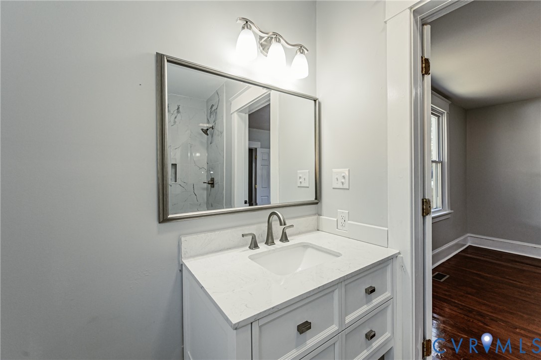 White cabinetry with a stone countertop, integrated sink, framed rectangular mirror, and three-light fixture