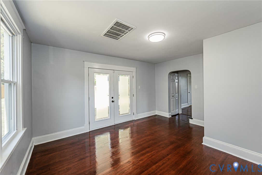 Interior space featuring wood-finish flooring, glass-panel French doors, an arched doorway, and a flush-mount ceiling light fixture