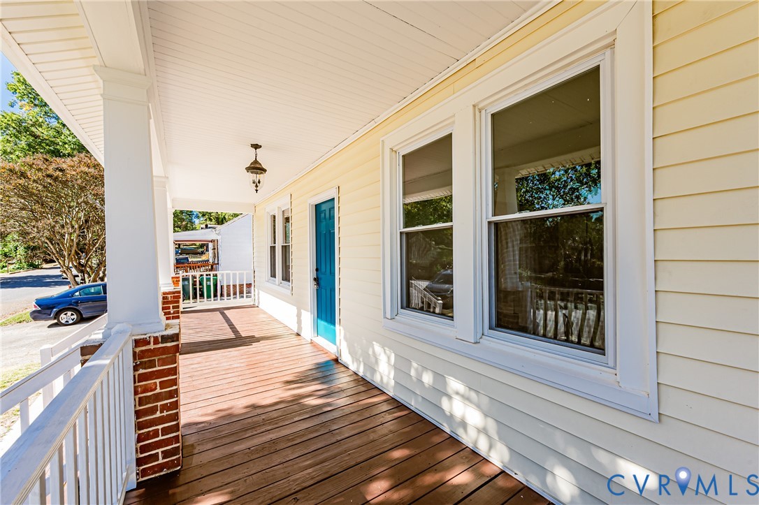 Covered front porch featuring wood-finish decking, white railings, brick-based columns, and horizontal lap siding