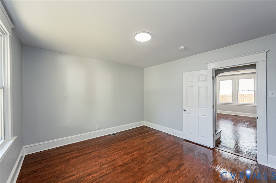 Interior room featuring wood-finish flooring, white six-panel door, neutral wall paint, and traditional door casing