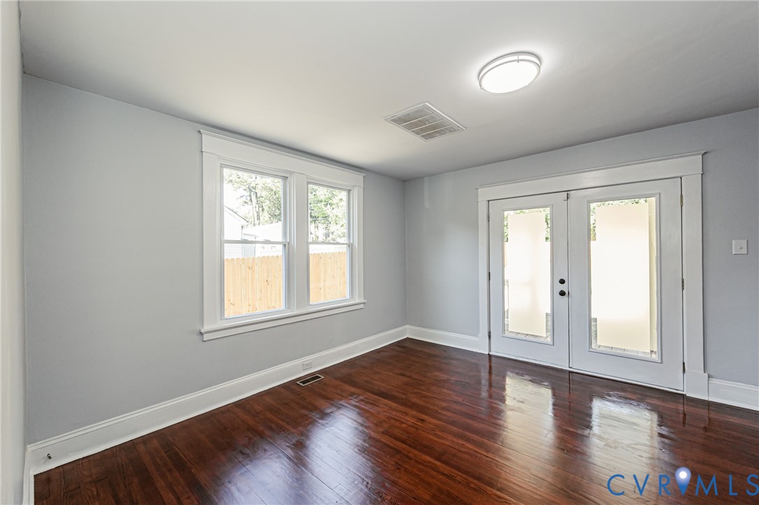 Room featuring wood-finish flooring, dual-pane windows with casing, and glass-paneled double doors with trim