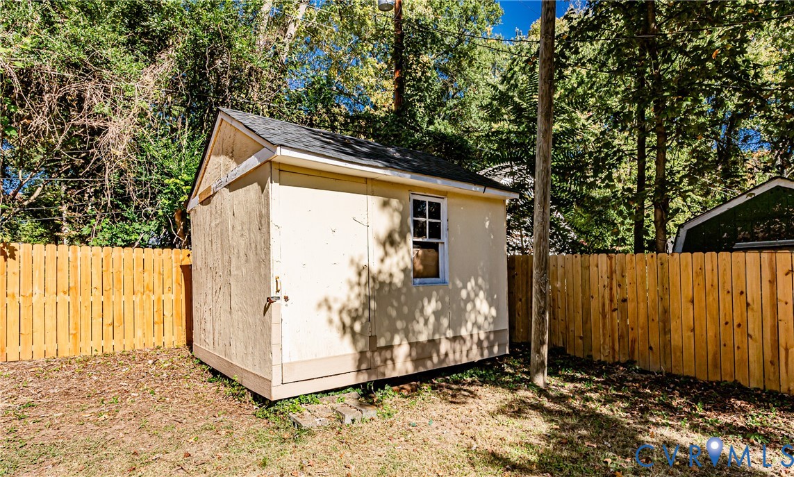 Detached storage structure featuring a gable roof, wood-composite siding, single window with muntins, and a privacy wood fence