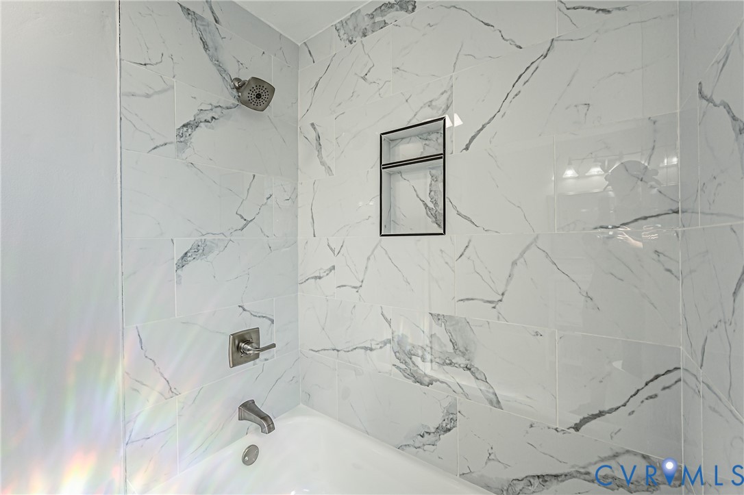 Bathtub surround featuring large-format veined tile, brushed metal fixtures, and a recessed built-in shower niche