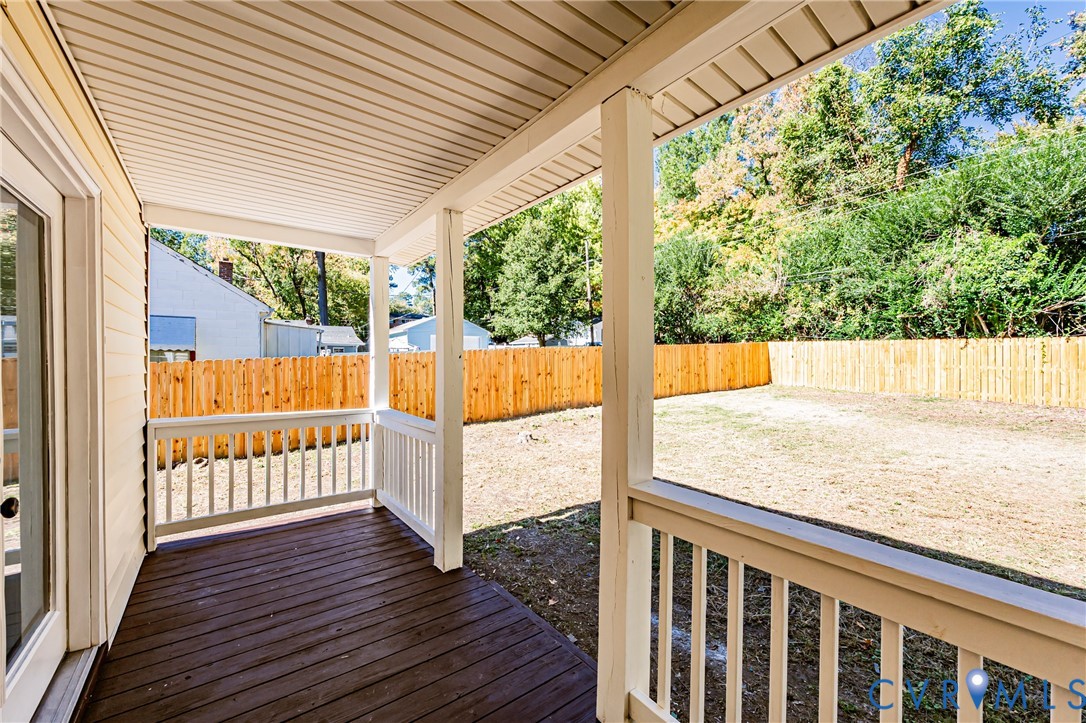 Covered wooden deck featuring white railings and a fenced backyard