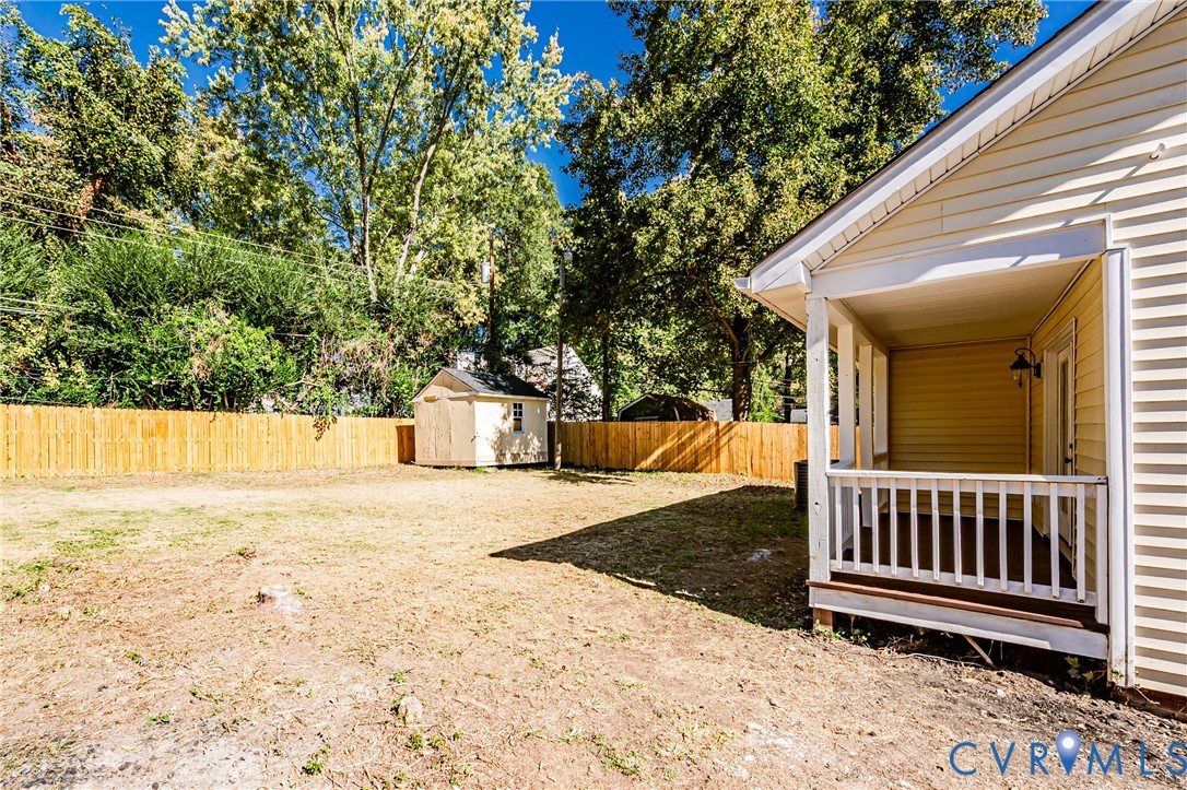 Rear exterior featuring a covered porch with white railing, a wood-slat privacy fence, and a detached storage shed