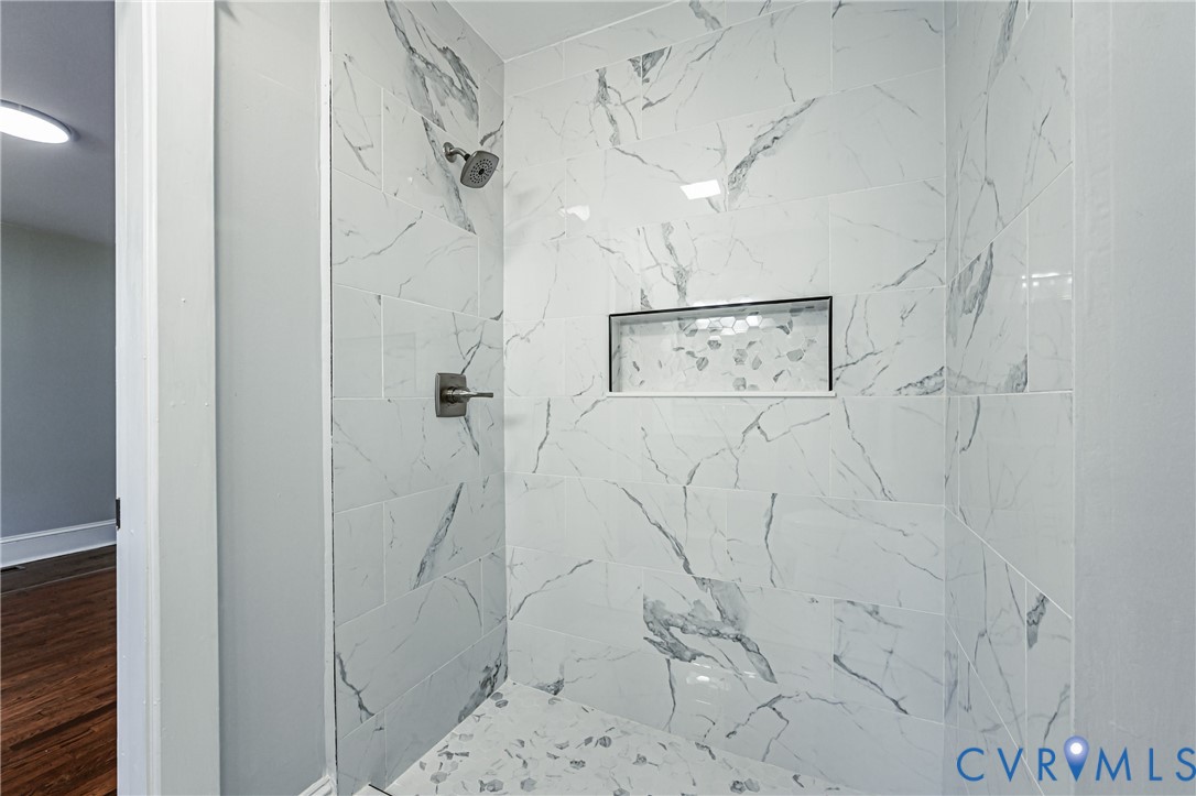 Walk-in shower featuring large-format stone-patterned tile, integrated recessed shelving, and a metal rainfall showerhead with a matching wall-mounted control valve