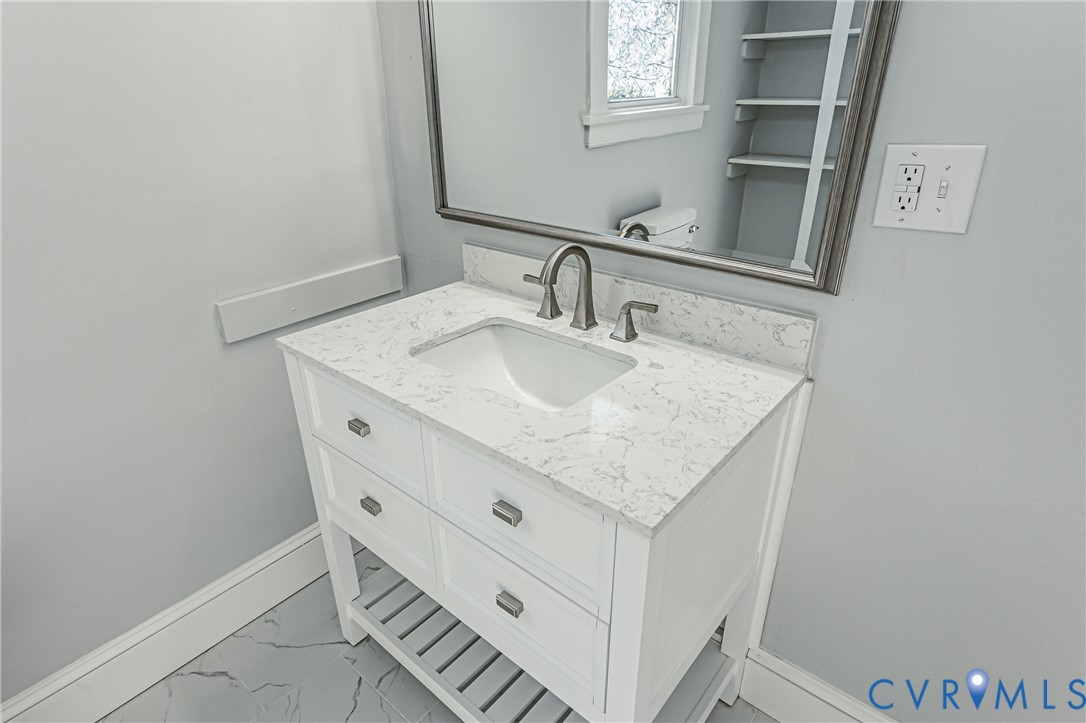 White vanity featuring a stone-composite countertop, undermount sink, metallic faucet, integrated lower shelving, and a framed mirror