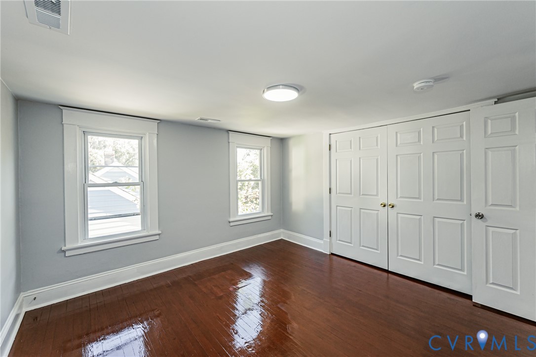 Interior space featuring wood-finish flooring, white six-panel closet doors, and windows framed by white millwork