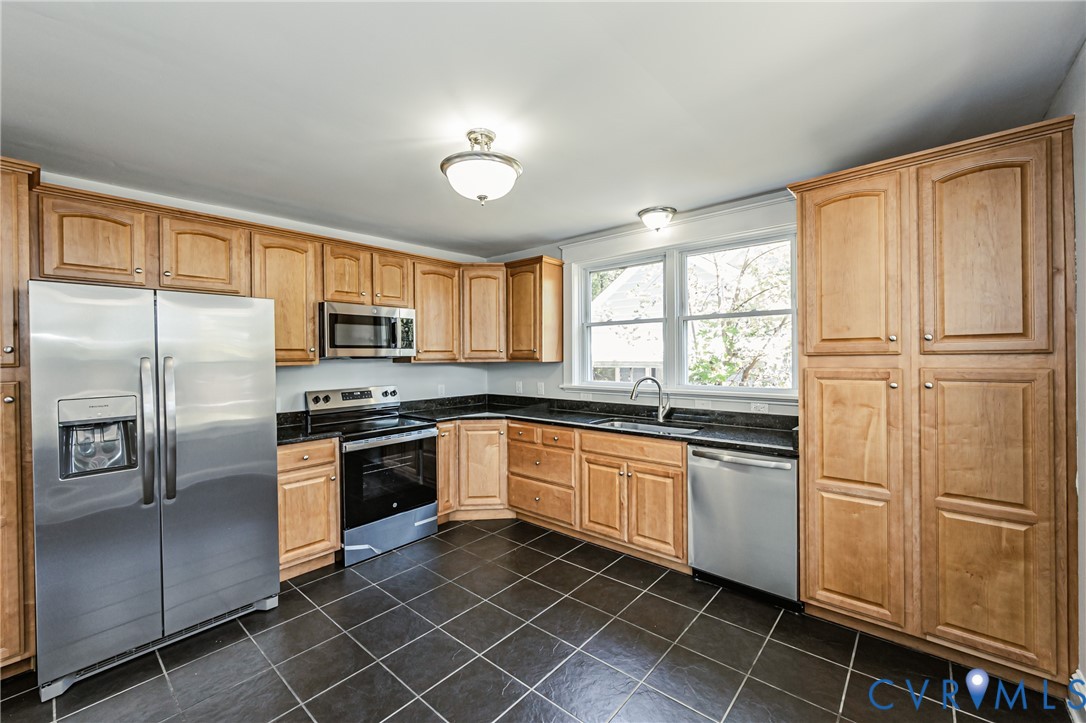 Kitchen featuring light wood cabinetry, dark stone countertops, stainless steel appliances, and dark tile flooring