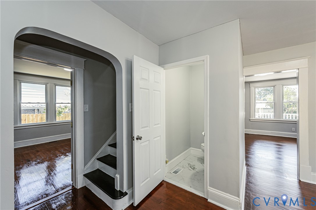 Arched entryway, solid wood-finish flooring, and multi-panel interior door with a classic white finish