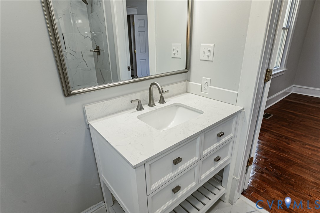 White vanity cabinet featuring a quartz countertop, an undermount rectangular sink, and brushed metal hardware, complemented by a silver-framed mirror and a wall-mounted faucet