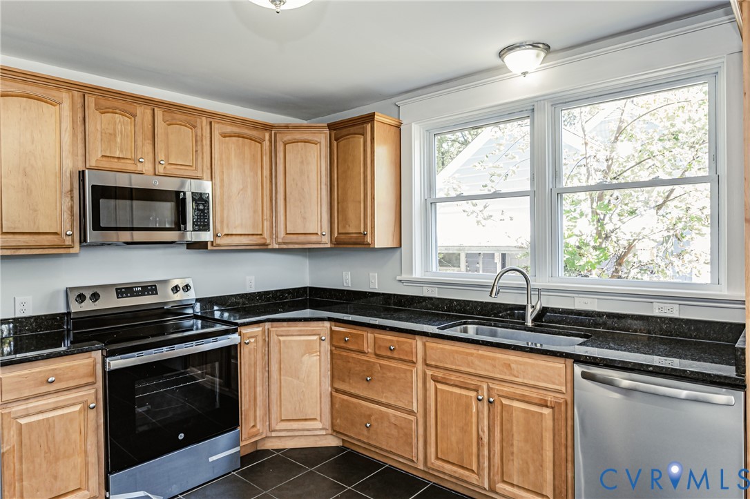 Kitchen featuring natural wood-finish cabinetry, dark solid-surface countertops, stainless steel appliances, a deep undermount sink with a gooseneck faucet, and tiled flooring