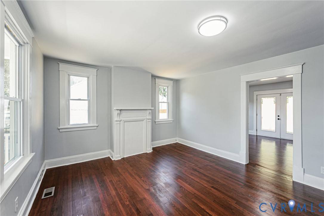 Interior space featuring wood-finish flooring, a decorative fireplace mantel, white window casings, and a double-door entrance with glass inserts