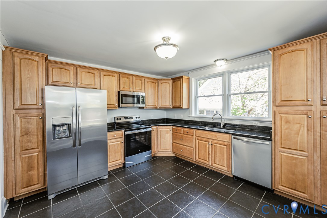 Kitchen featuring light-finish cabinetry, dark stone countertops, stainless steel appliances, tile flooring, and a double-basin sink