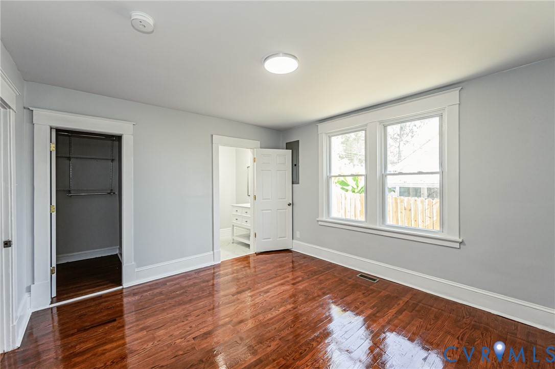 Room featuring polished wood-finish flooring, white door and window casing, dual-pane windows, and a walk-in closet