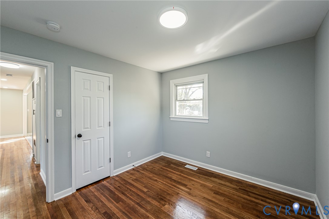 Neutral-toned interior space featuring wood-finish flooring, a single-panel window, a white six-panel door, and a flush-mount overhead light fixture