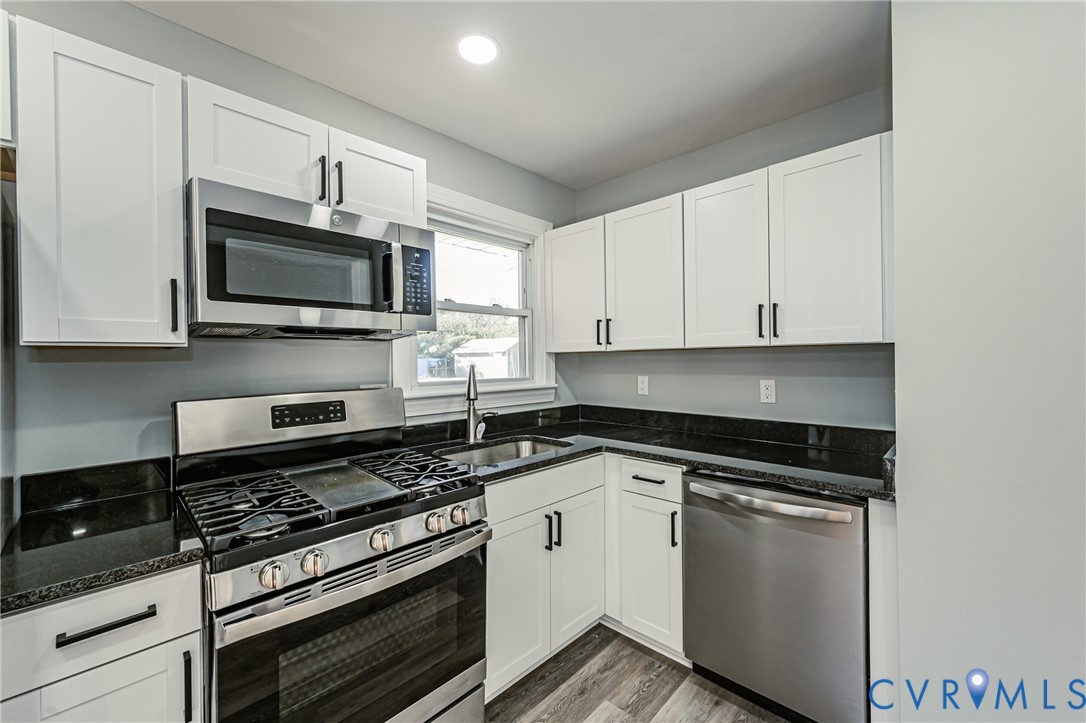 Kitchen featuring white cabinetry, dark stone countertops, stainless steel appliances, and wood-finish flooring