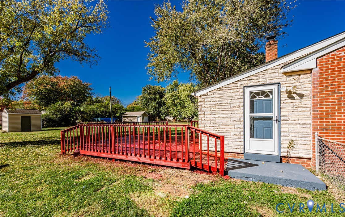 Exterior features include a red-painted wood deck, brick and stone masonry siding, a single-story storage shed, and a fenced yard